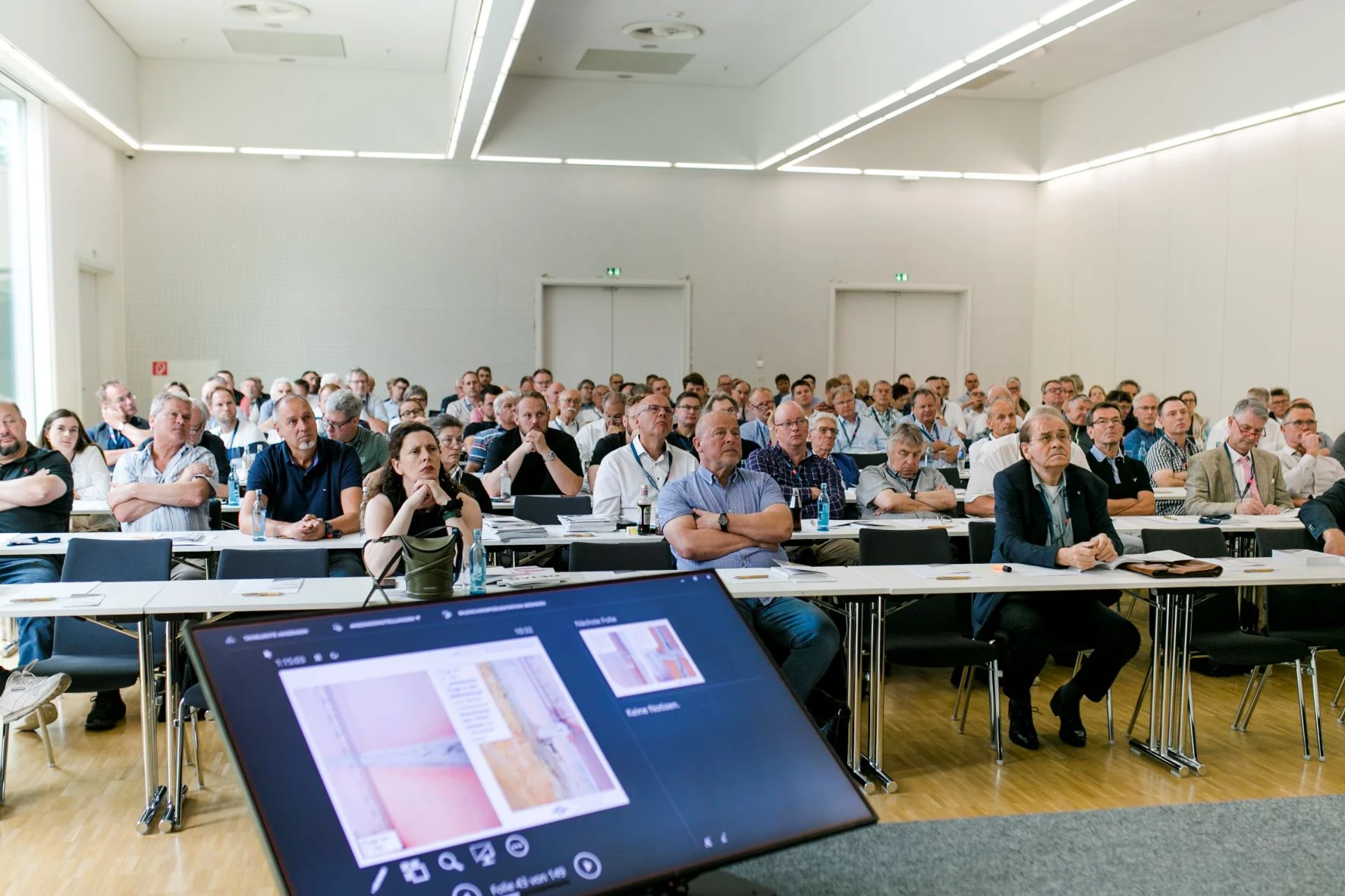 EIPOS Sachverständigentage Sachverstand am Bau 2023 - Blick auf die Teilnehmer von der Bühne am Monitor für die Sprecher vorbei