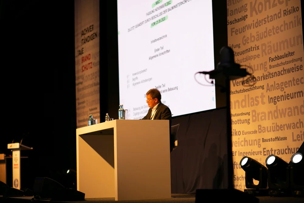 EIPOS Sachverständigentage Brandschutz 2021 - Referent auf der Bühne mit Folien im Hintergrund