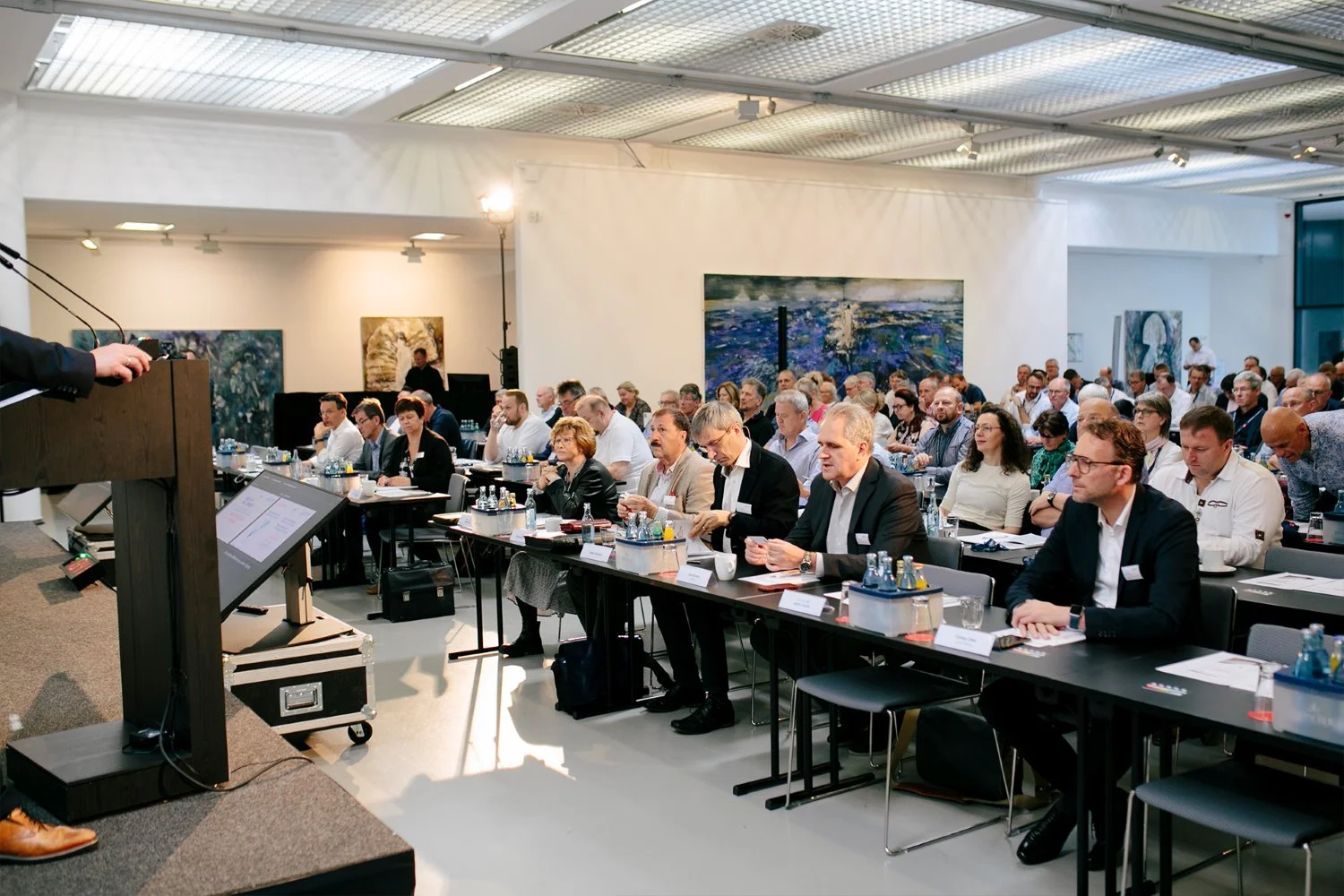 Blick von einer Position seitlich neben der Bühne ins zuhöhrende Publikum, während eines Vortrags