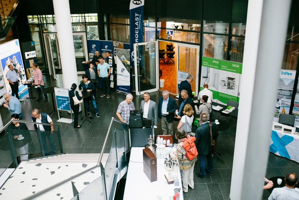 Aufnahme von der Treppe oben in die Fachausstellung mit Teilnehmern und Standbertreuern im Gespräch