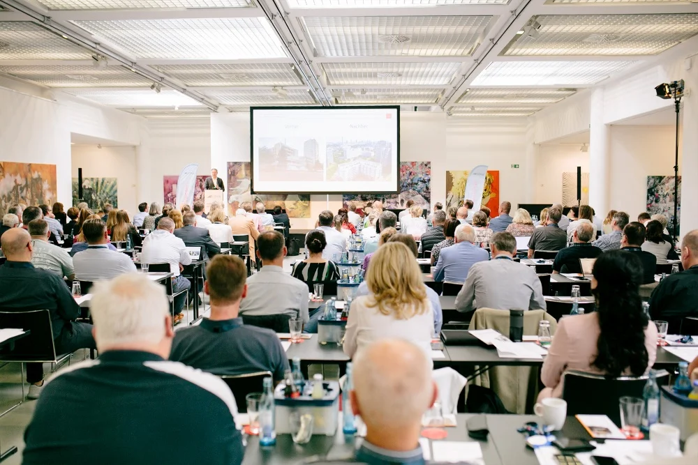 Blick von hinten, über das Publikum zur Bühne mit einer Präsentation über Immobilien